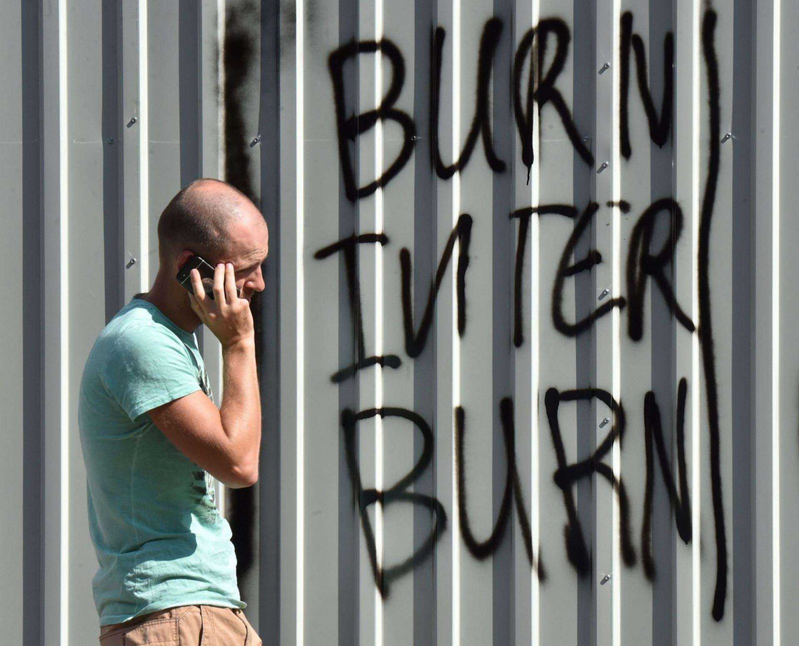 An activist speaks on his mobile phone as he walks graffiti that reads, "Burn Inter, burn"  on a protective barricade placed at the entrance of the TV channel "Inter" during a protest by activists in Kiev on September 5, 2016.  Activists, who accused Inter -- one of the biggest Ukrainian TV channels -- of a pro-Russian position and working for the Kremlin, blocked the channel's central office and the studios in order to hault its operation.  / AFP PHOTO / SERGEI SUPINSKY